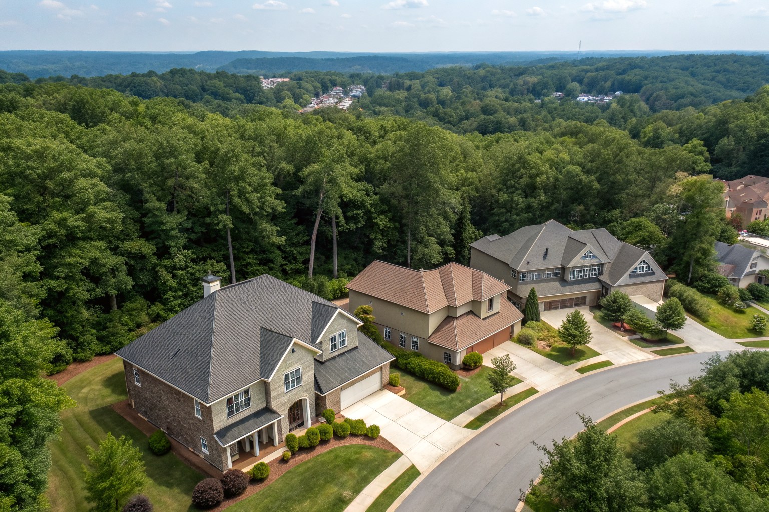 Aerial view of two-story homes with gray and brown shingle roofs along a curving street in a wooded subdivision
