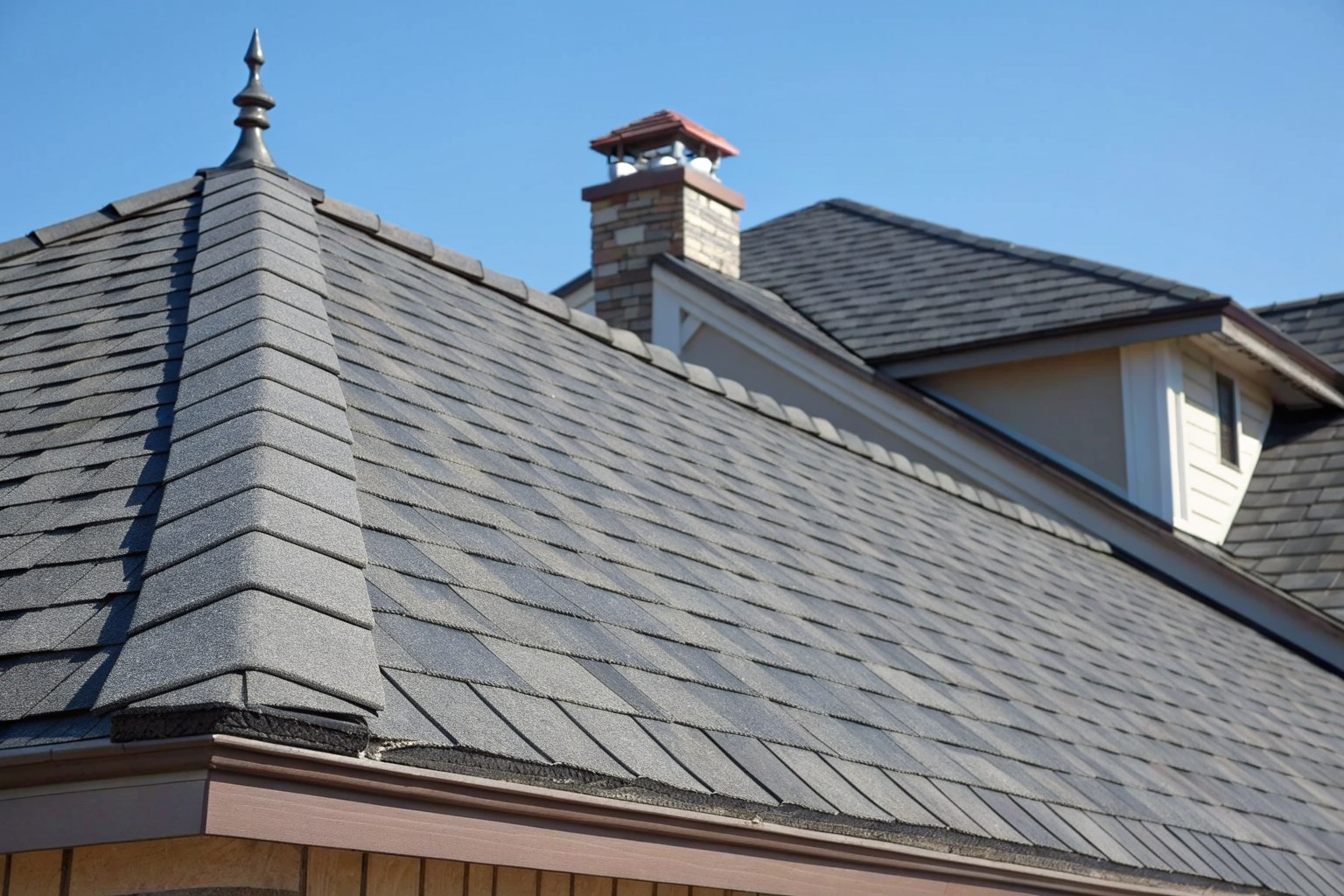 A new charcoal architectural shingle roof with a straight ridge cap against blue sky